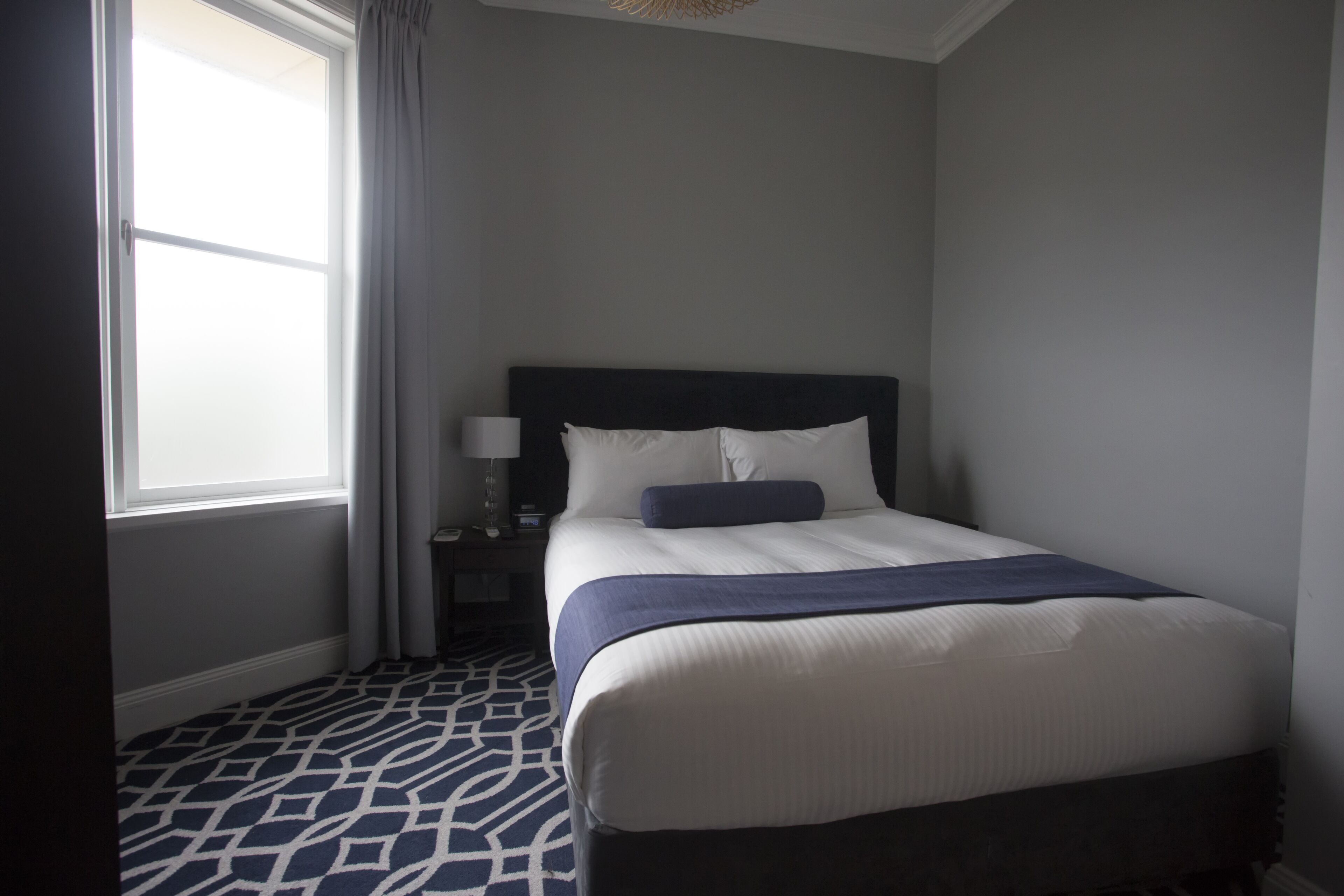 Een hotelkamer met een groot bed, een nachtkastje, een lamp en een raam met gordijnen.