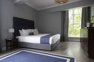 Un dormitorio con una cama grande, una mesita de noche, una lámpara, un aparador y una ventana con cortinas.