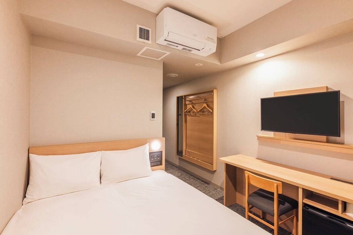 Una habitación de hotel con cama, escritorio, silla, televisor y armario.