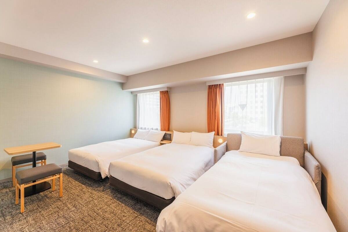 Una habitación de hotel con dos camas individuales, una mesita y un banco.