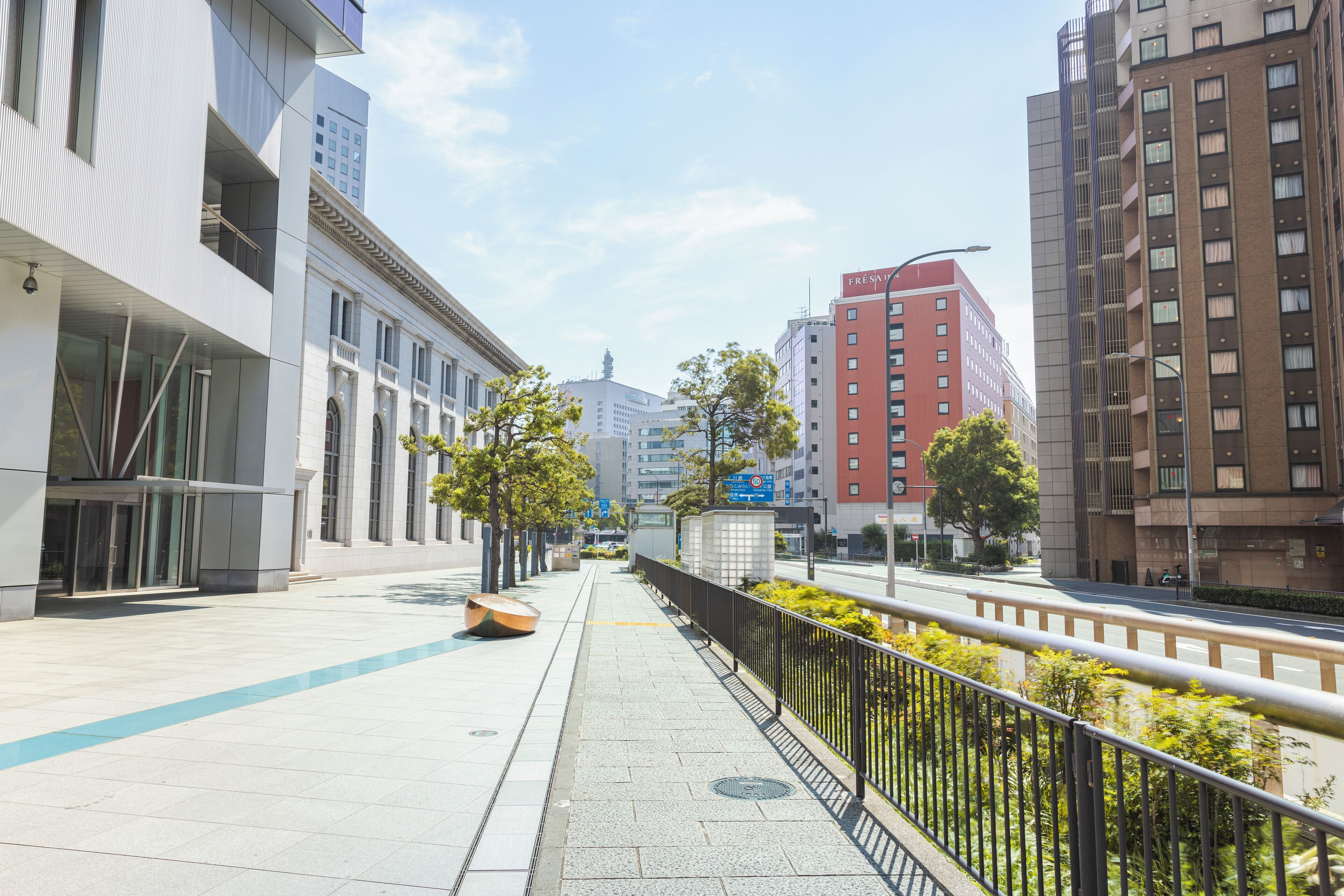 Een moderne stadstraat met trottoirs, gebouwen en een heldere lucht.