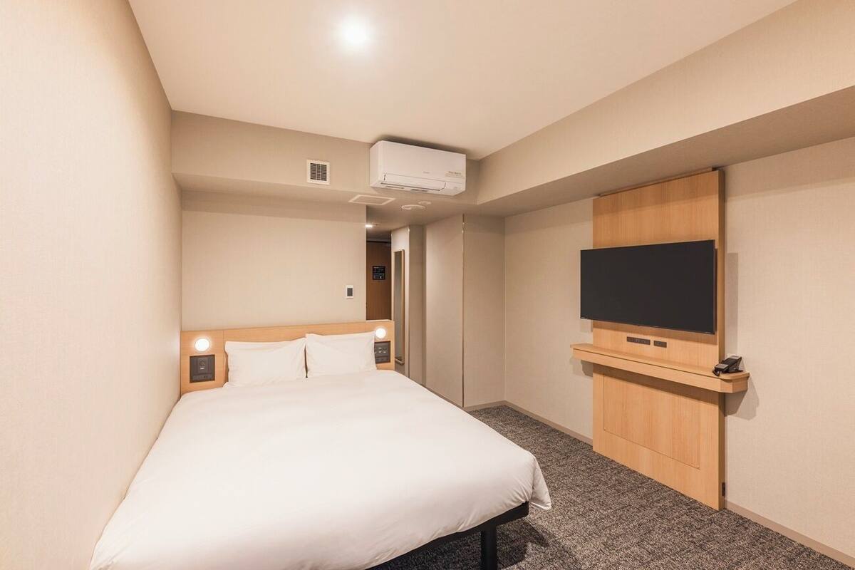 Habitación de hotel con una cama, un televisor de pantalla plana montado en la pared y un mueble de madera pequeño debajo del televisor.