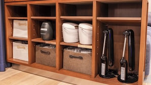 Un mueble de almacenamiento de madera con varios compartimentos, incluyendo una sección con un vaporizador facial y dos recipientes blancos.