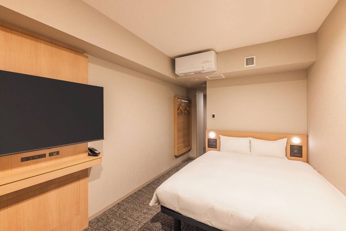 Habitación de hotel con cama, televisor sobre un soporte de madera, armario y aire acondicionado instalado en la pared.
