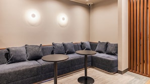 Un área de espera moderna con un sofá modular, dos mesas redondas, luces empotradas en el techo y un separador de madera.
