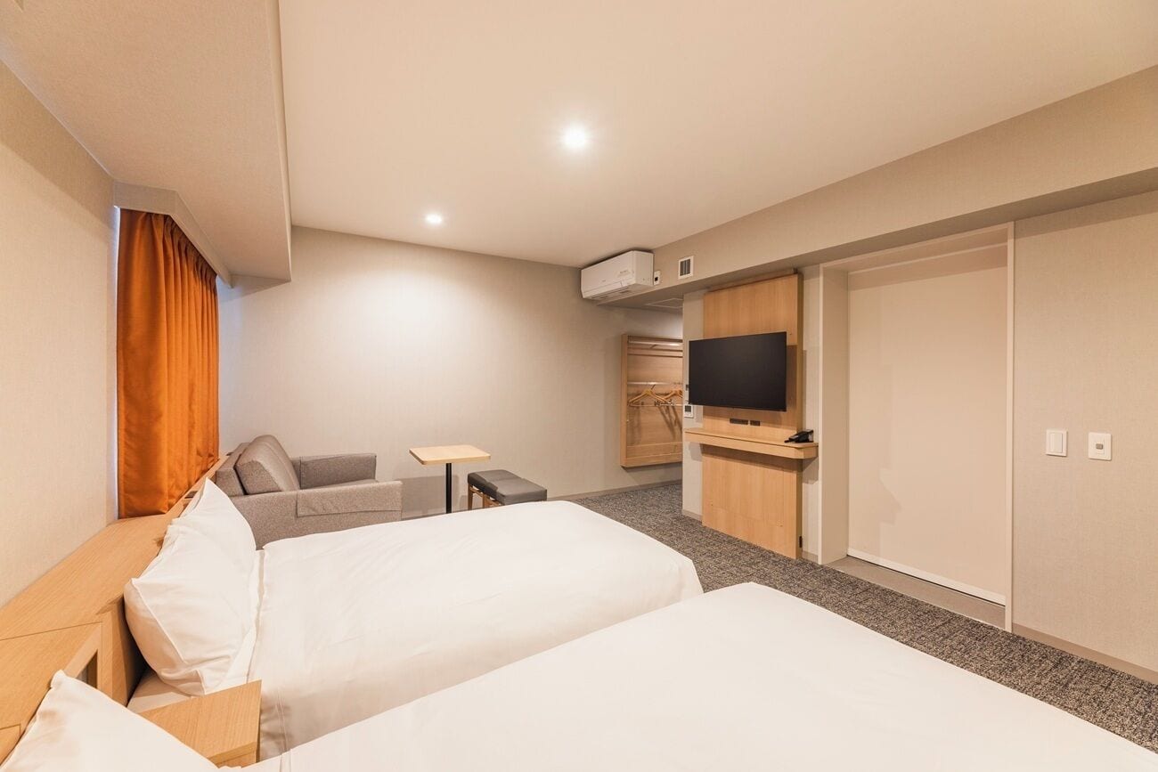 A hotel room with two beds, a TV, a desk, and a wardrobe.