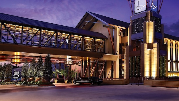 A modern hotel with a prominent tower featuring a clock, a covered walkway, and a well-lit entrance area.