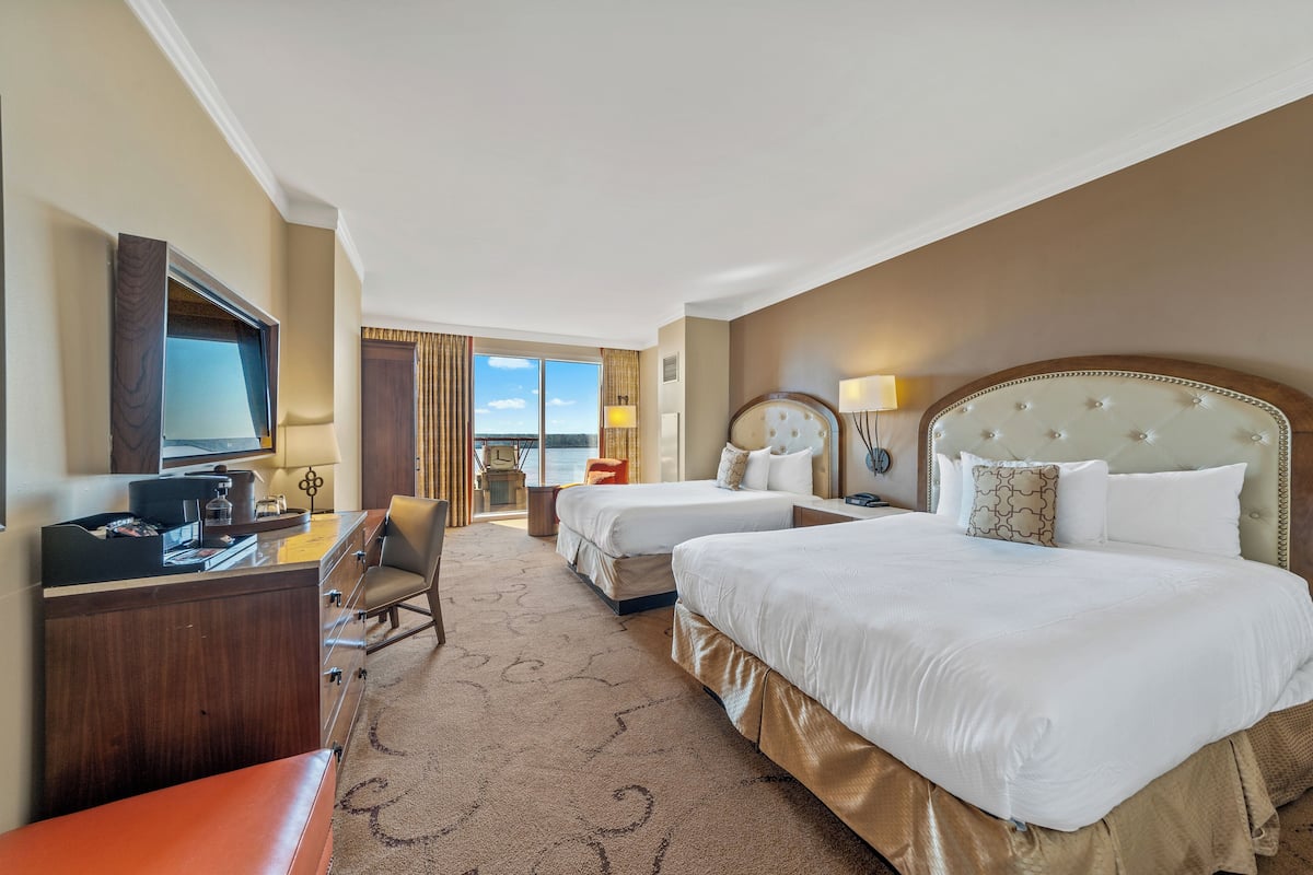 A hotel room with two beds, a desk with a computer, a chair, and a view of the outdoors.