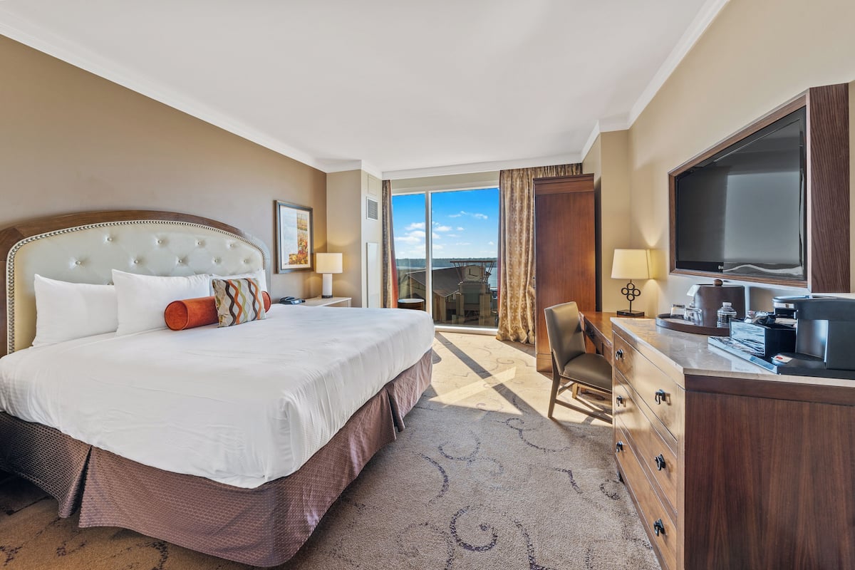 A hotel room with a large bed, a desk, a television, and a view of the outdoors.