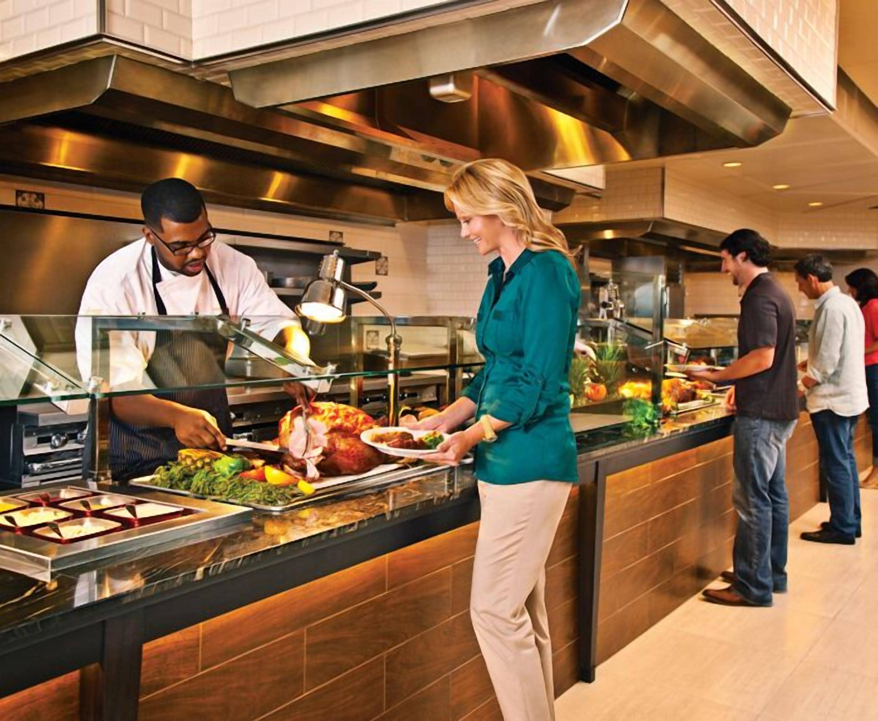 Montaje de bufé con diversos alimentos, incluyendo un pavo asado, en una cocina moderna.