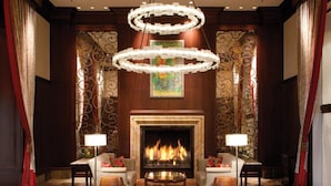 A hotel lobby with a stone-tiled floor, a central fireplace, and two sofas with lamps.