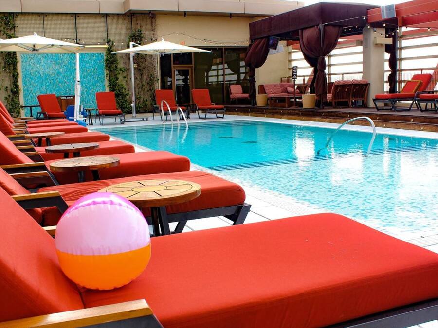 Un área junto a la piscina con sillas de descanso rojas y una piscina pequeña.