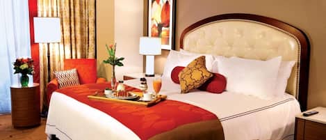 A hotel room with a large bed, a bedside table with a lamp, a vase with flowers, and a painting on the wall.