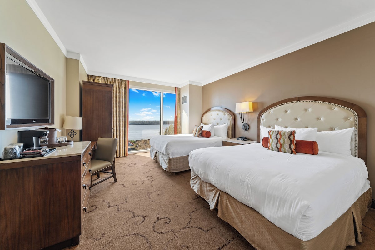 A hotel room with two beds, a desk, a TV, and a view of the ocean.