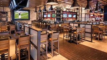 A restaurant with multiple bar areas, wooden tables and chairs, and a large TV screen displaying sports.