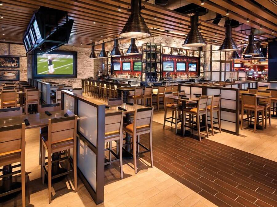 A restaurant with multiple bar areas, wooden tables and chairs, and a large TV screen displaying sports.