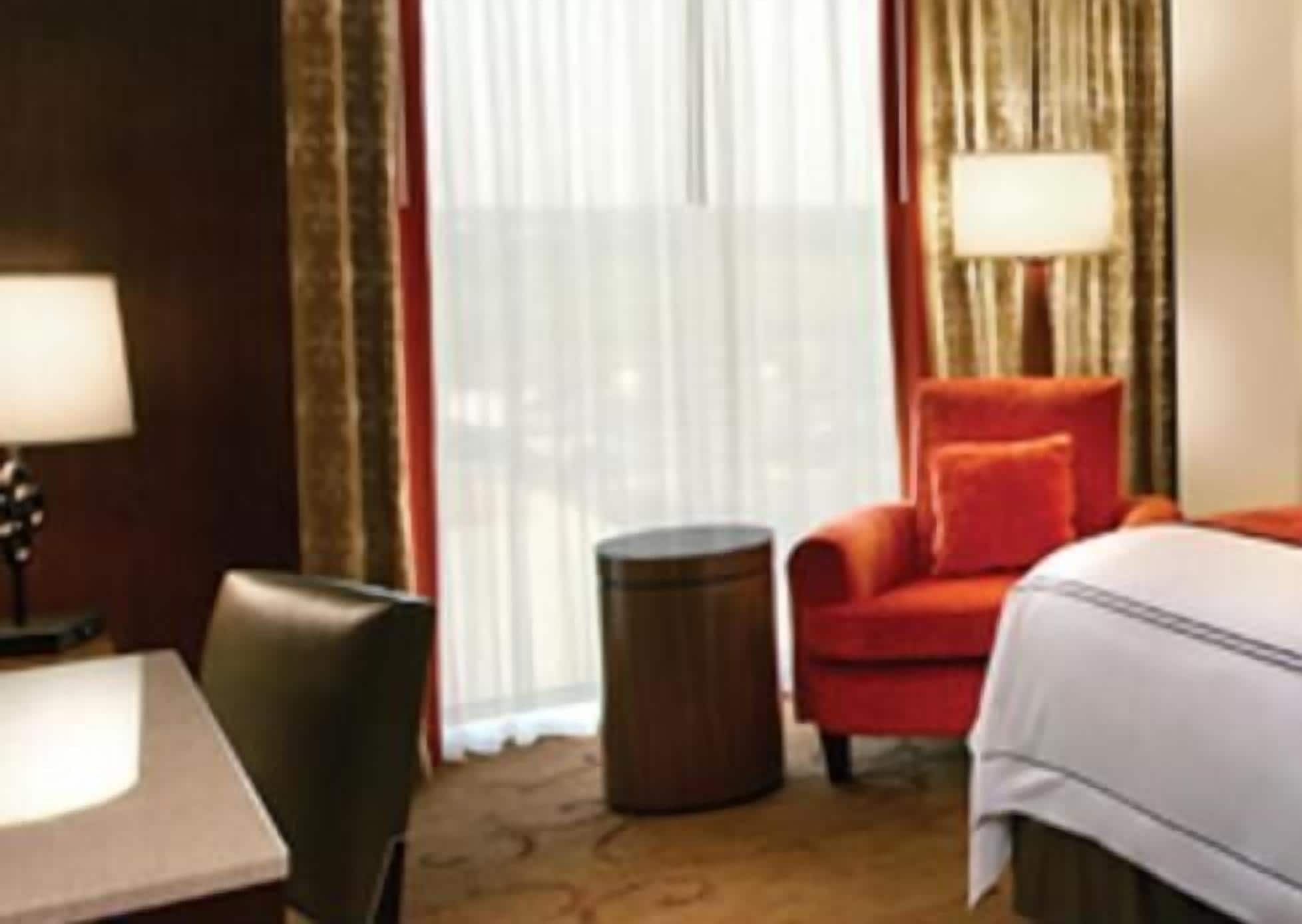 A hotel room with a bed, a desk, a chair, a small round table, and a window with curtains.