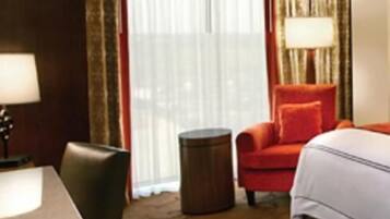 A hotel room with a bed, a desk, a chair, a small round table, and a window with curtains.