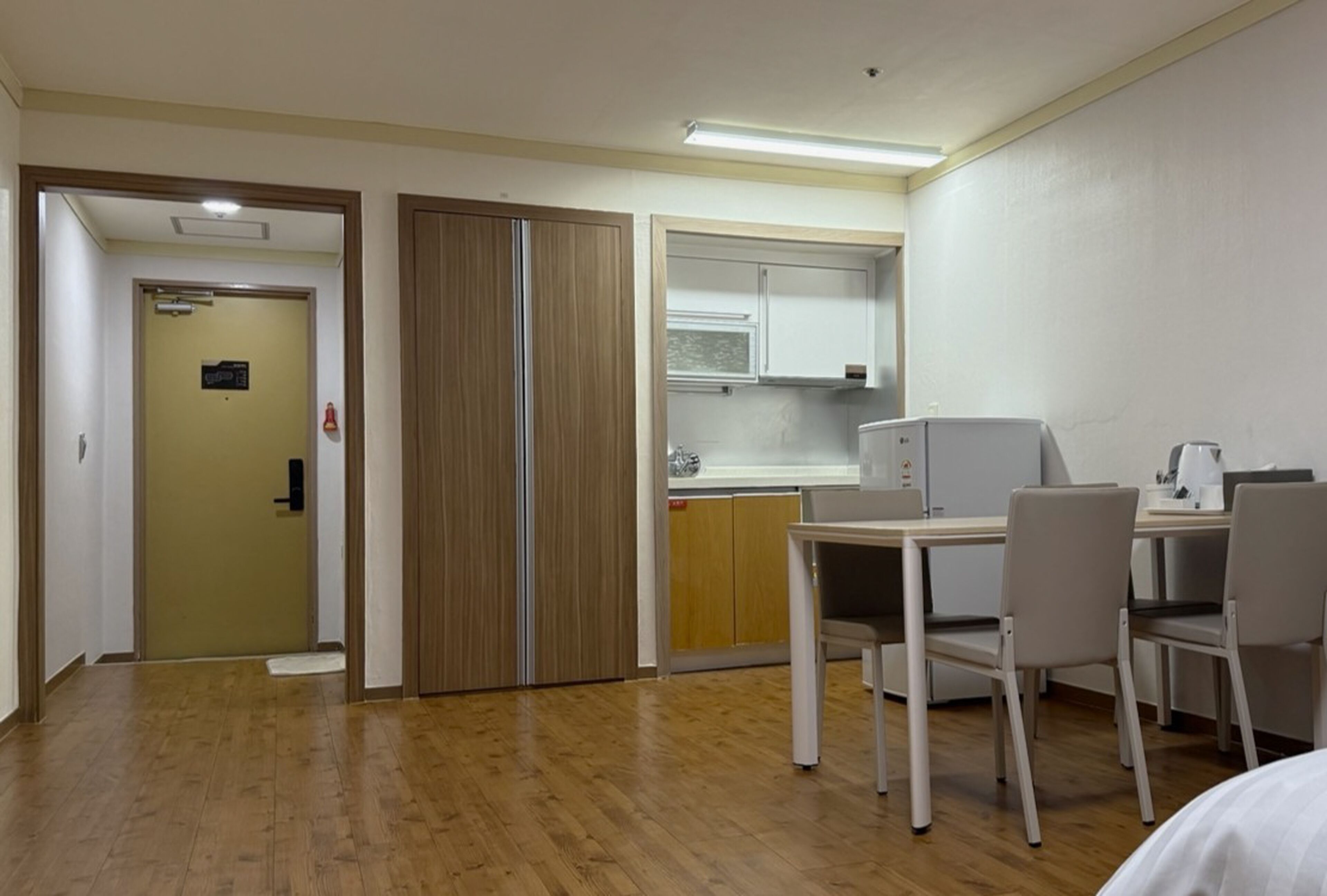 A hotel room with a wooden floor, a desk with two chairs, a kitchenette with a microwave, and a wardrobe.
