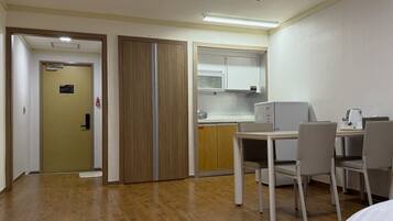 A hotel room with a wooden floor, a desk with two chairs, a kitchenette with a microwave, and a wardrobe.