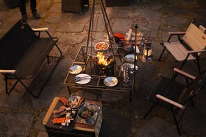 An outdoor dining setup with a grill, dining table, chairs, and various food items.