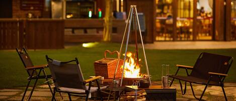 An outdoor seating area with foldable chairs, a fire pit, and a table with a drink.