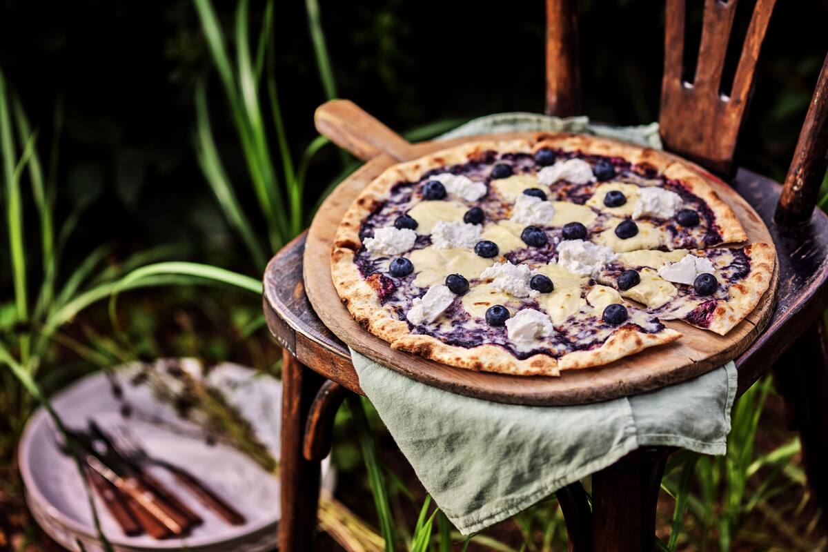 A pizza on a wooden board placed on a chair with a green cloth.