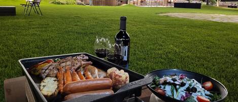 An outdoor dining area with a grill, a bottle of wine, and a salad bowl.
