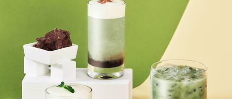 Three layered drinks on white stands against a green and beige background.