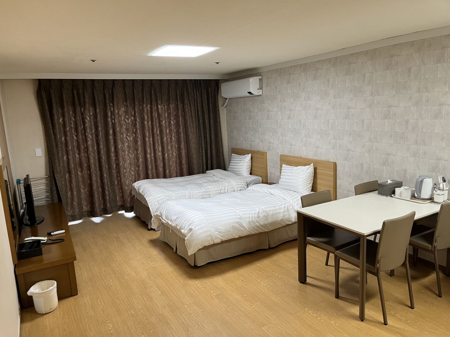 Habitación de hotel con dos camas, un escritorio y una silla. Hay un cubo de basura y un televisor sobre un soporte.