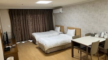 Habitación de hotel con dos camas, un escritorio y una silla. Hay un cubo de basura y un televisor sobre un soporte.