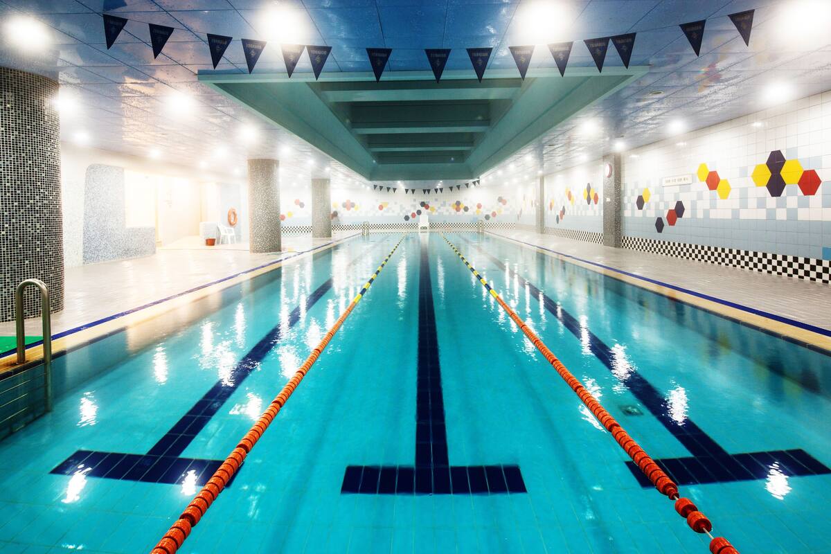 A long swimming pool with lane dividers, tiled walls, and a ceiling with lights.