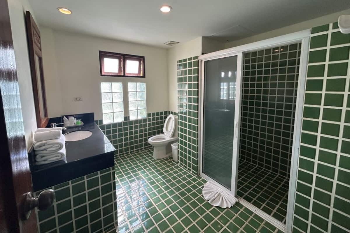 A bathroom with green tiled walls, a black sink, a toilet, and a shower enclosure.