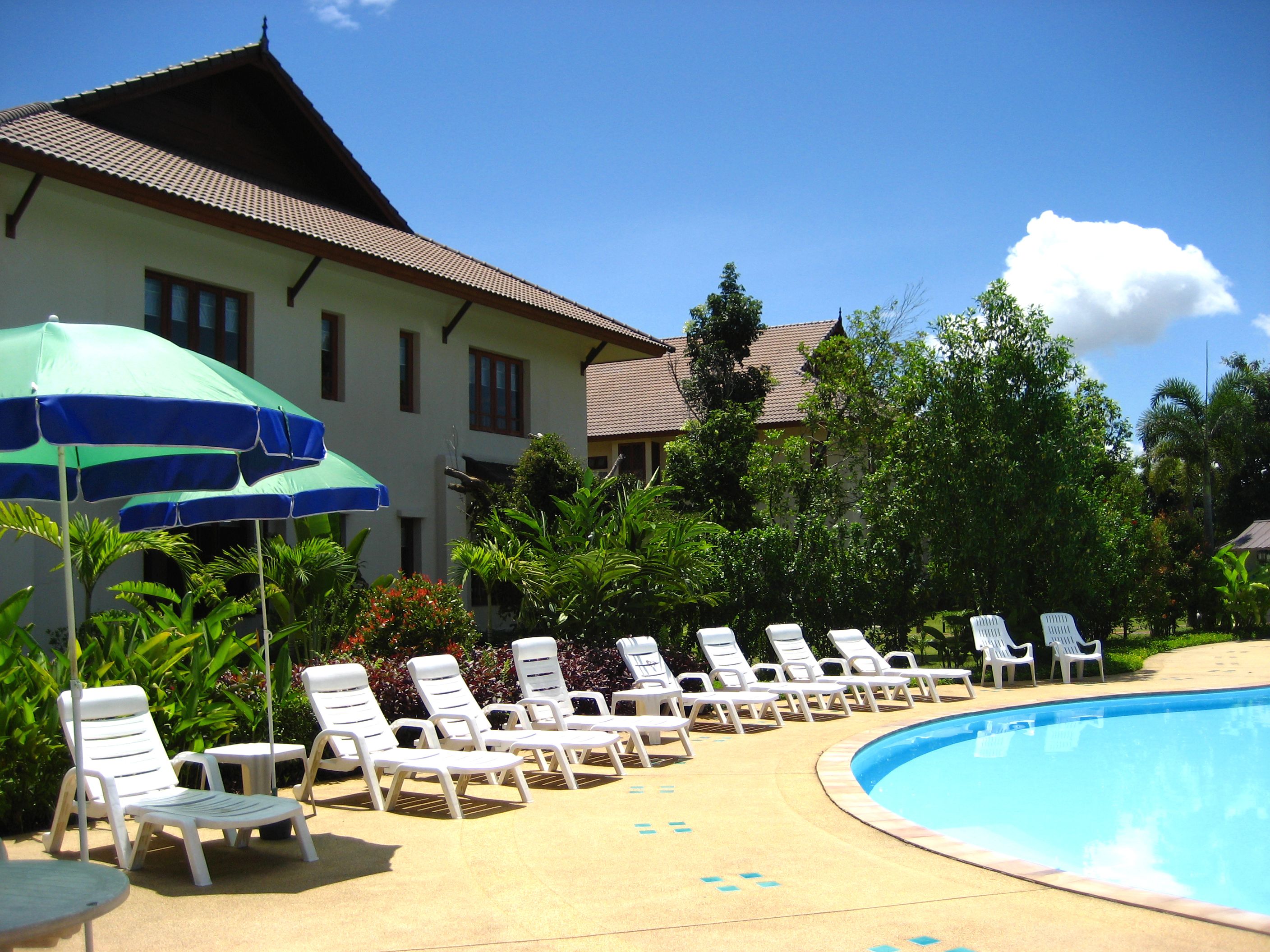 A pool area with white lounge chairs and a blue umbrella.