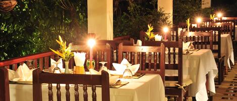 A restaurant with tables set for dining, surrounded by greenery and illuminated by warm lighting.