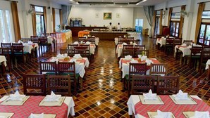 A spacious dining hall with multiple tables and chairs, a central counter, and large windows.