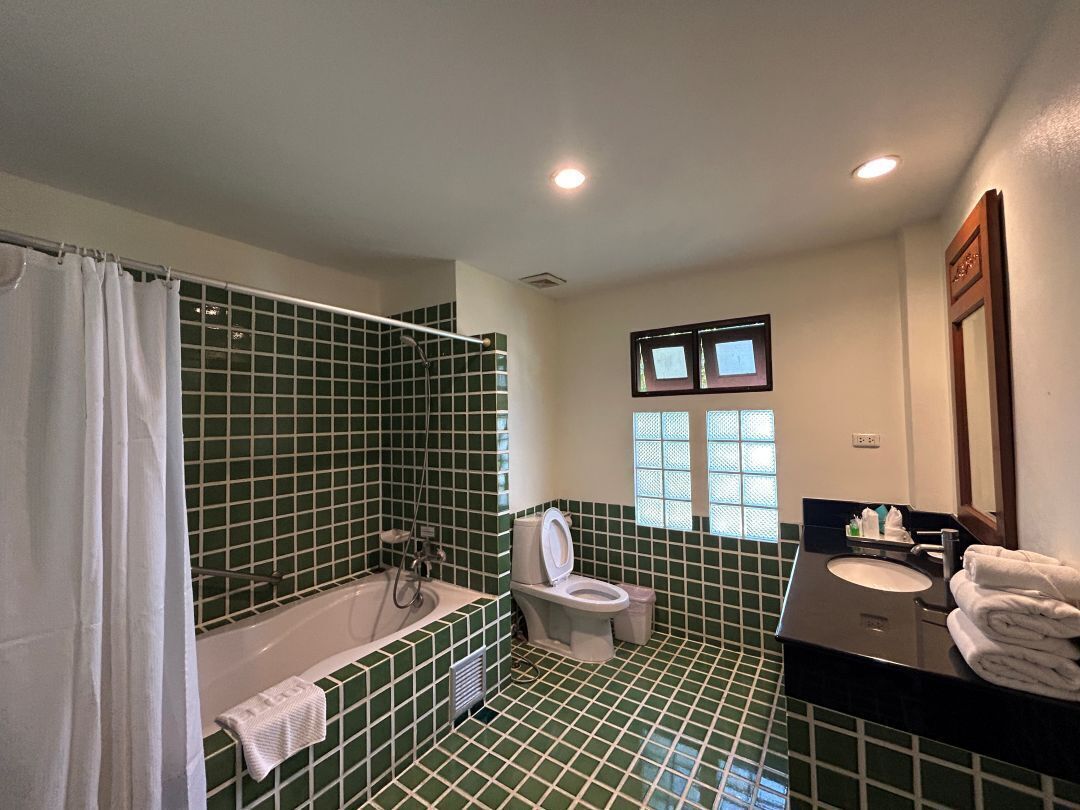 A bathroom with green tiles, a bathtub, a toilet, a sink, and a window with blinds.