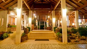 A covered outdoor area with steps leading to a building entrance, surrounded by potted plants and decorative elements.