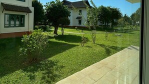 A view from a balcony overlooking a well-maintained lawn with a house and a tree in the background.