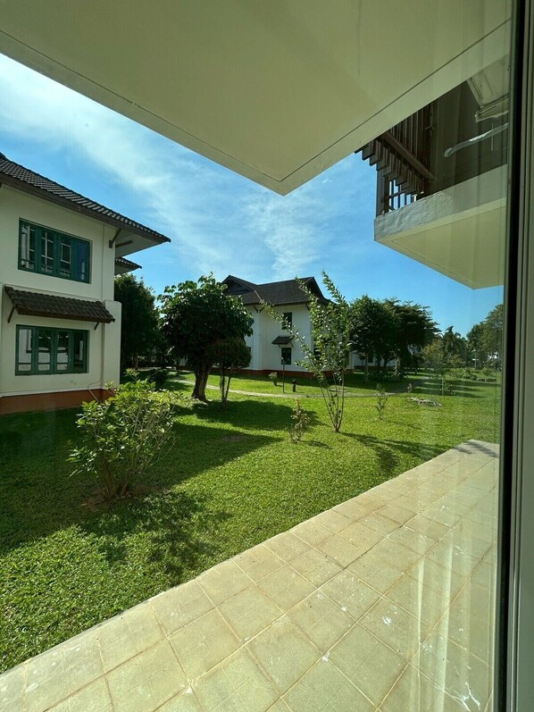 Blick vom Balkon auf eine gepflegte Rasenfläche mit einem Haus und einem Baum im Hintergrund.