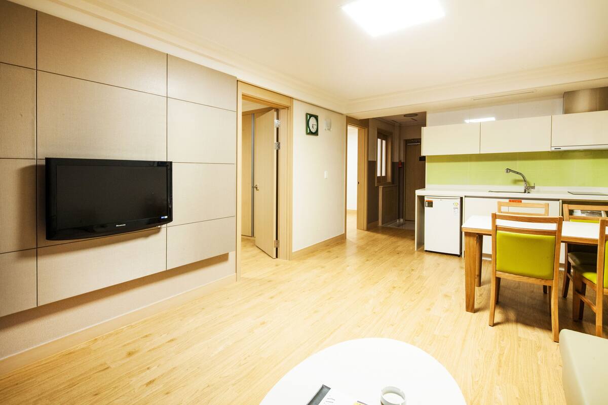A modern kitchen with wooden cabinets, a built-in TV, and a dining area with a table and chairs.