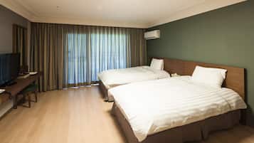 A hotel room with two beds, a desk with a chair, a television, and a large window with curtains.