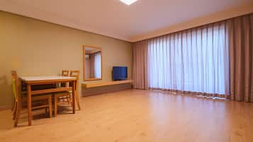 A room with a wooden dining table, chairs, a television on a stand, a large window with curtains, and a mirror on the wall.