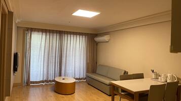 A hotel room with a sofa, a round wooden table, a coffee maker, and a TV on the wall.