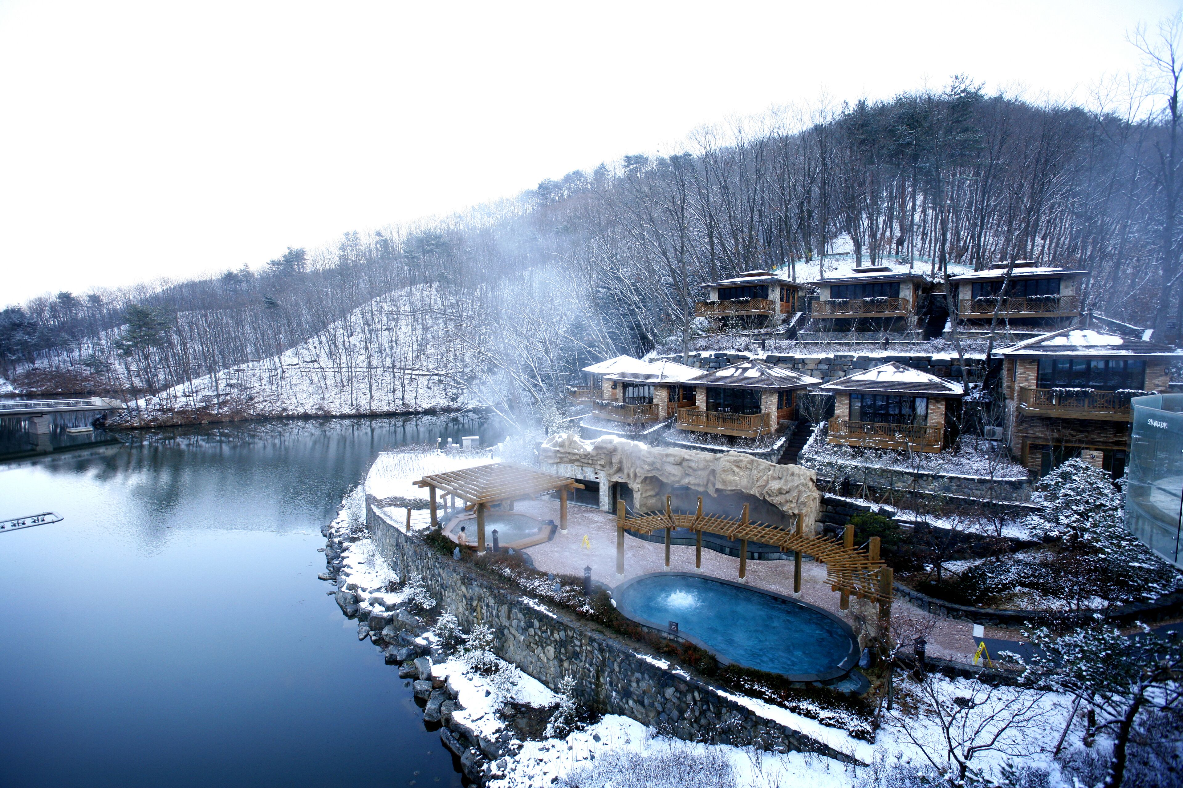 Un resort de varios pisos con piscina, terraza de madera y alrededores nevados.