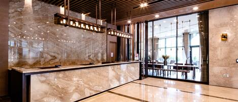 A modern reception area with a marble counter, wooden ceiling beams, and large windows.