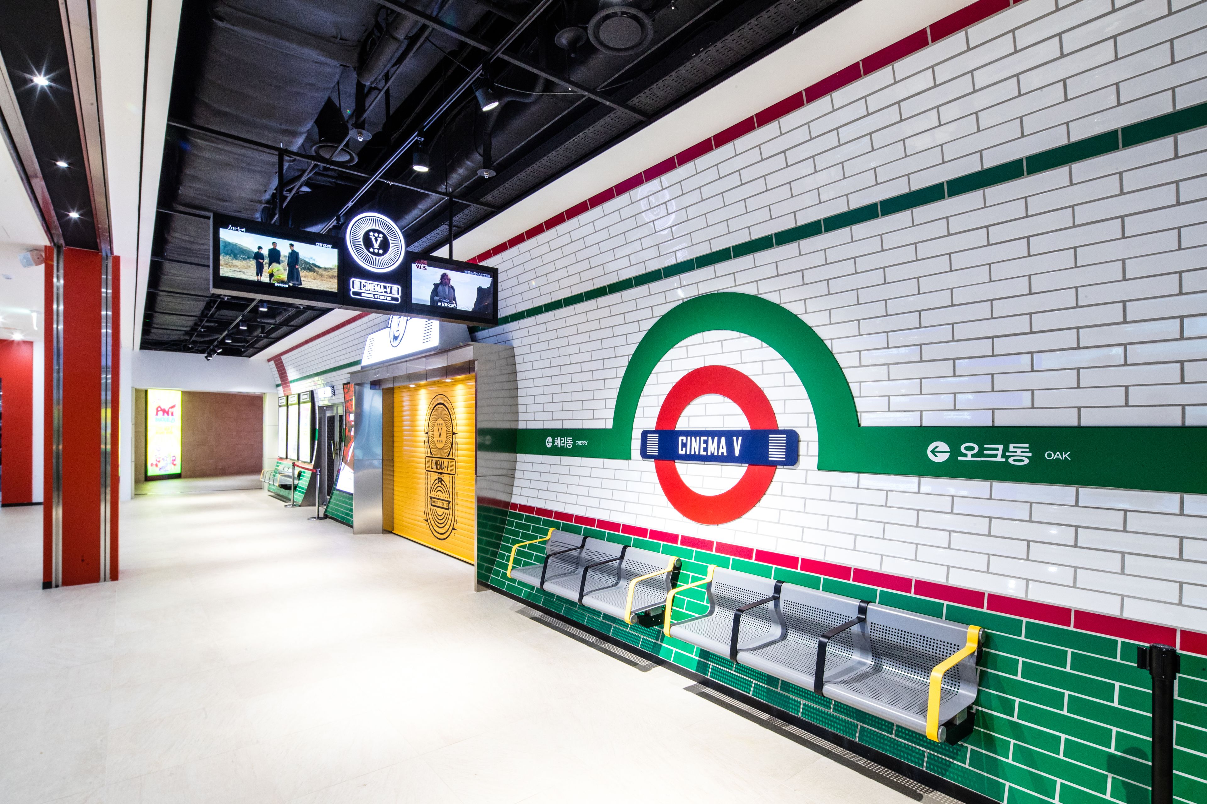 A subway station with a cinema V sign, seating areas, and a digital display.