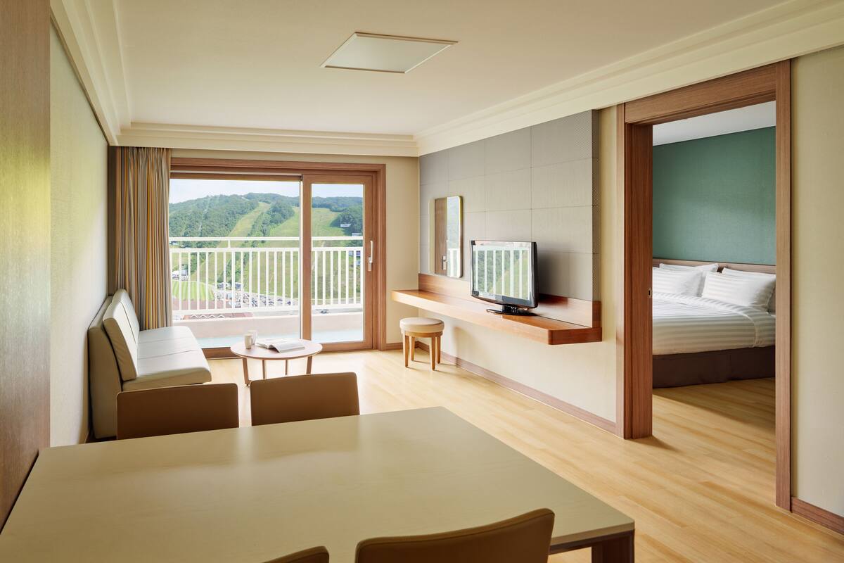 A hotel room with a balcony, a TV, a bed, a dining area, and a small table.