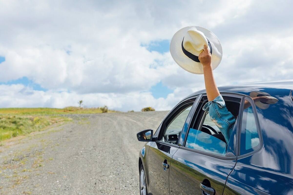 A person holding a hat on the side of a car.