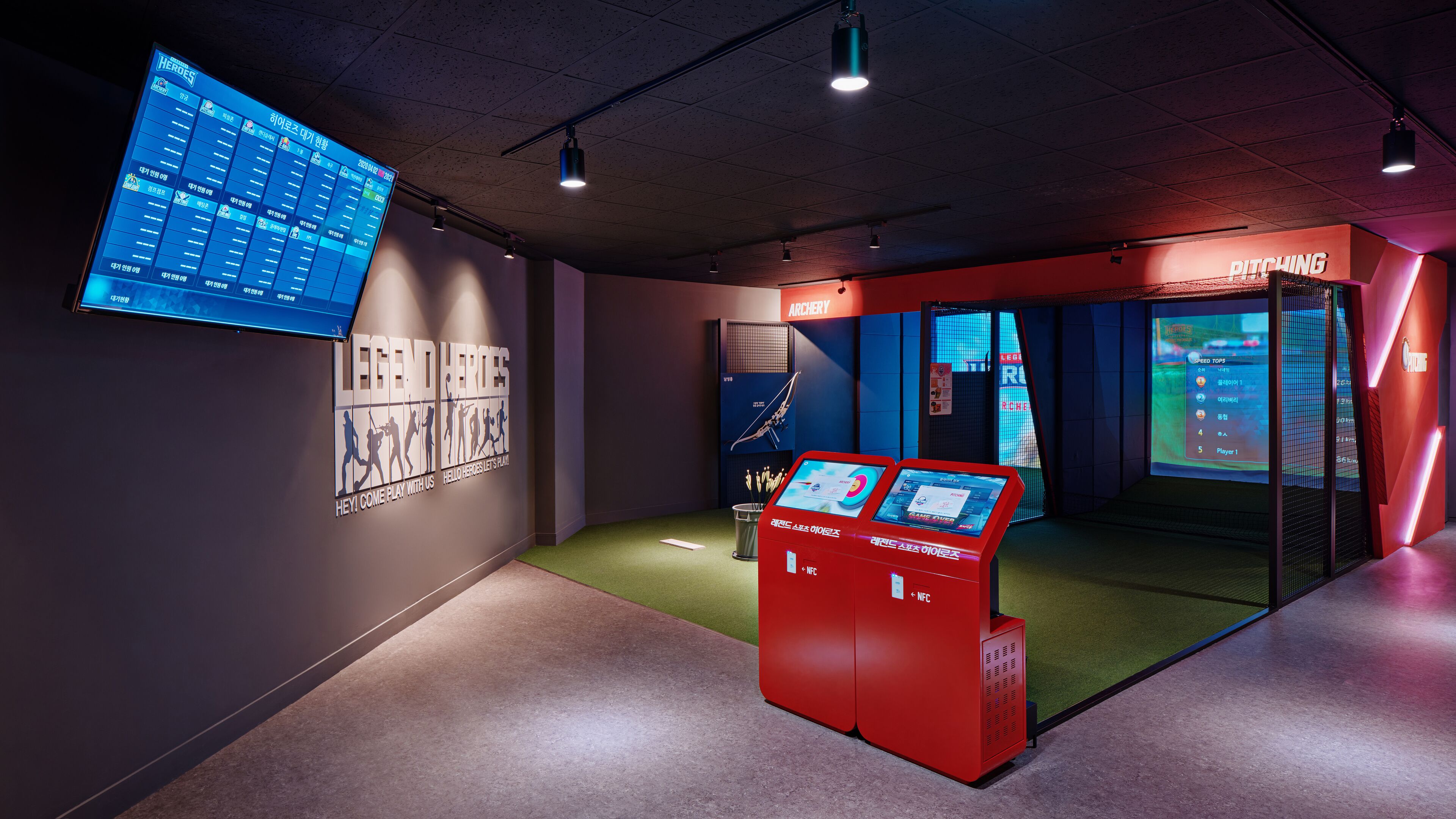 Un espace de jeux doté d’un grand écran affichant l’interface d’un jeu, d’un kiosque d’information rouge et d’une section intitulée « LANCER ».